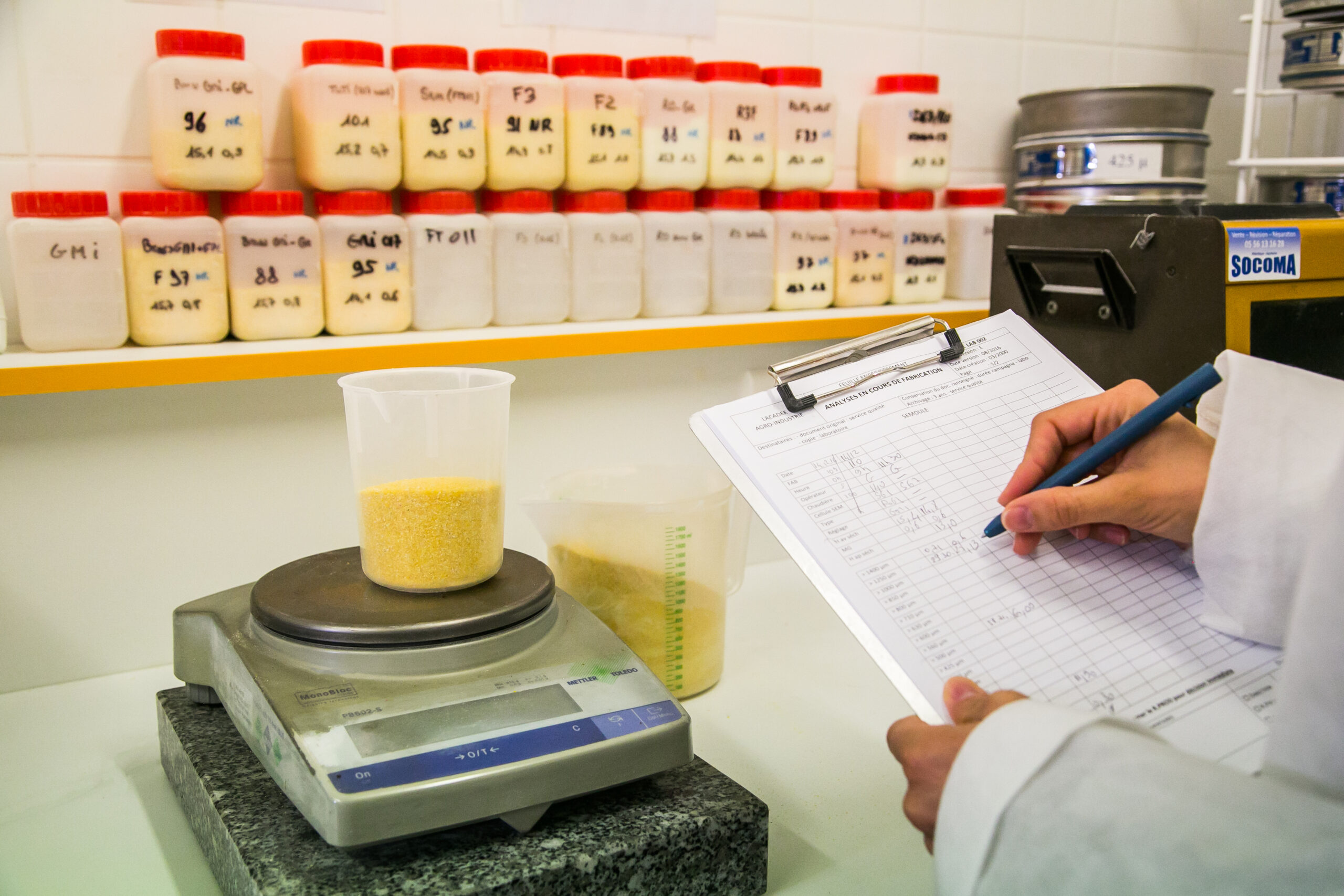 Technicienne réalisant le contrôle qualité et l'analyse d'échantillons de farine de maïs en laboratoire Lacadée.